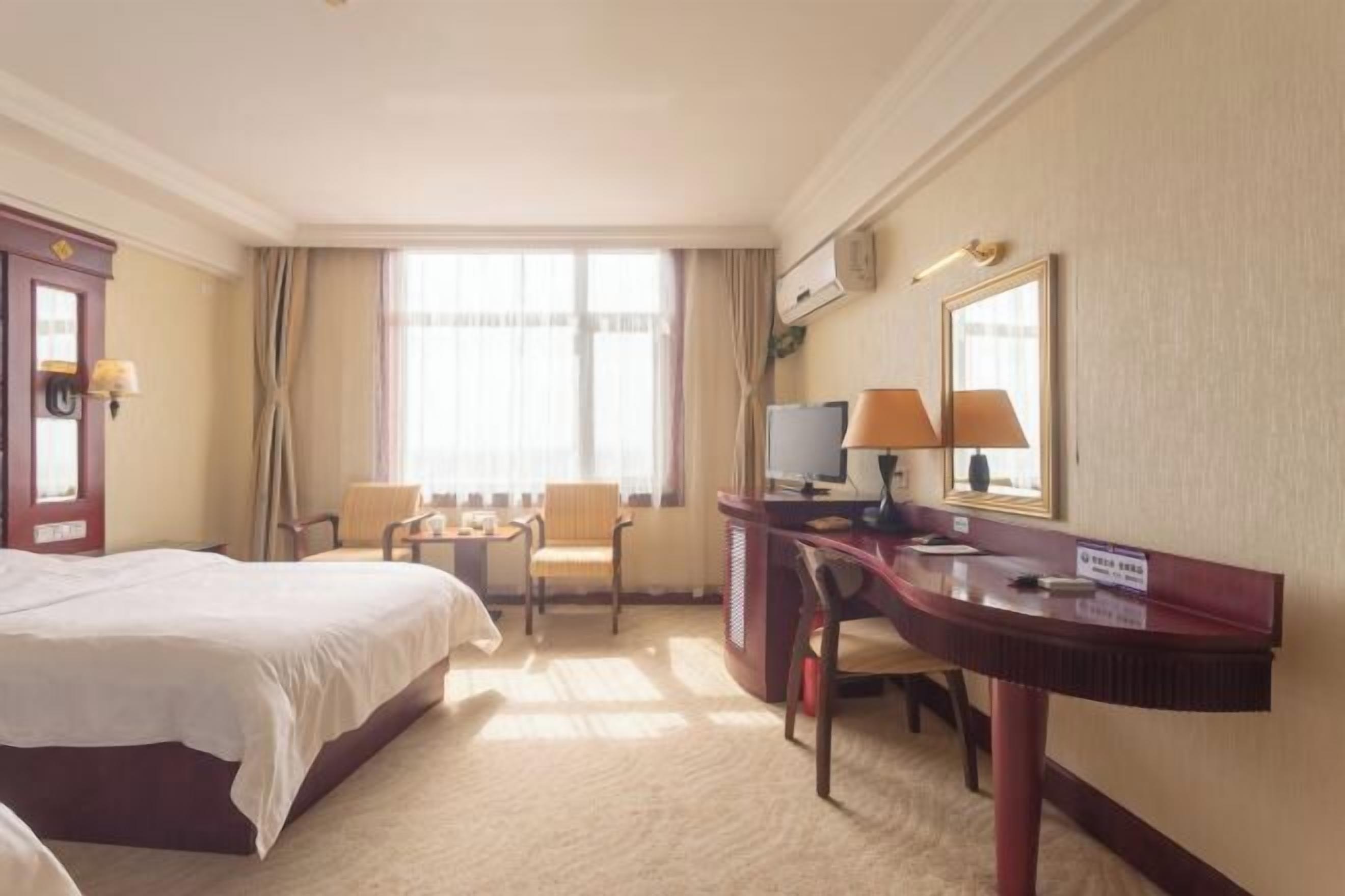 Una habitación de hotel con una cama grande, un escritorio con computadora, dos sillas y un ventanal con cortinas.