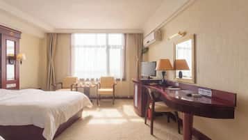 A hotel room with a large bed, a desk with a computer, two chairs, and a large window with curtains.