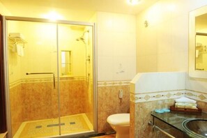A bathroom with a glass-enclosed shower, a toilet, and a sink with a glass countertop. - Dongfang Hotel (Rushan)