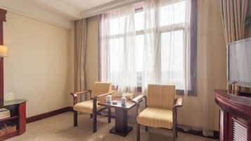 A hotel room with a large window, two armchairs, a small table with a teapot, and a television on a wooden stand.