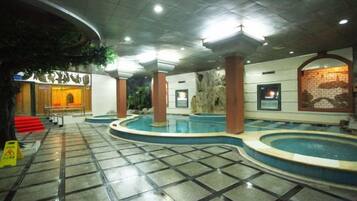 A hotel lobby with a large indoor pool, a reception desk, and a staircase leading to the upper floors.