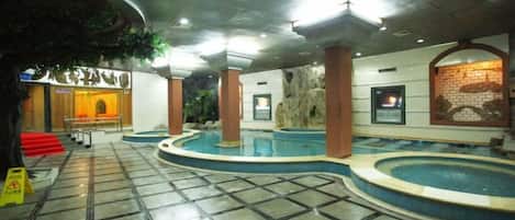 Un hall de hotel con una amplia piscina interior, un mostrador de recepción y una escalera que sube a los pisos superiores.