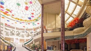Um amplo átrio com escadaria central, vários níveis e teto de vidro.
