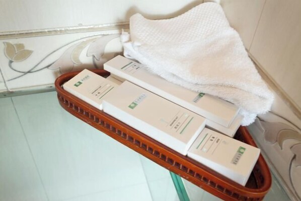 A bathroom with a white towel, a white bath mat, and a basket containing several white boxes. - Dongfang Hotel (Rushan)