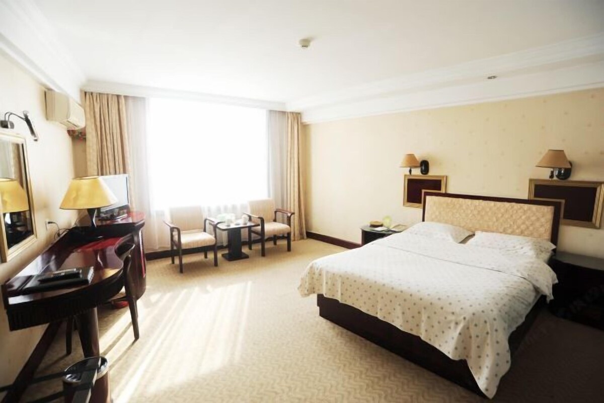 A hotel room with a bed, a desk, a chair, a small table, and a window with curtains.