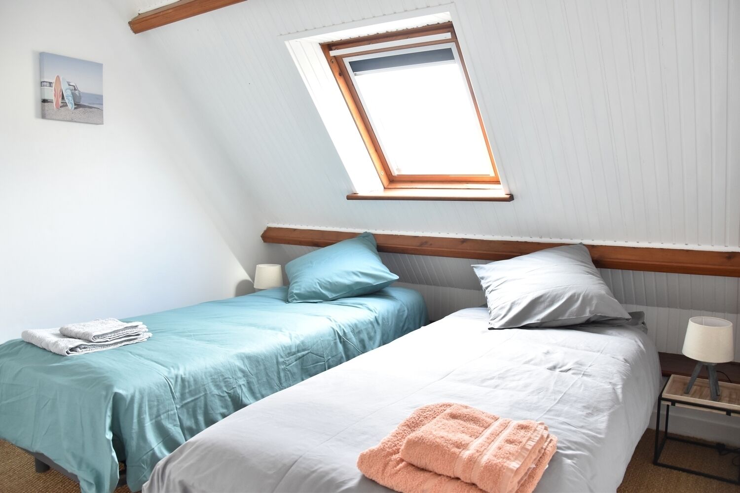 A room with two beds, a skylight, a small table, and a wall-mounted picture.