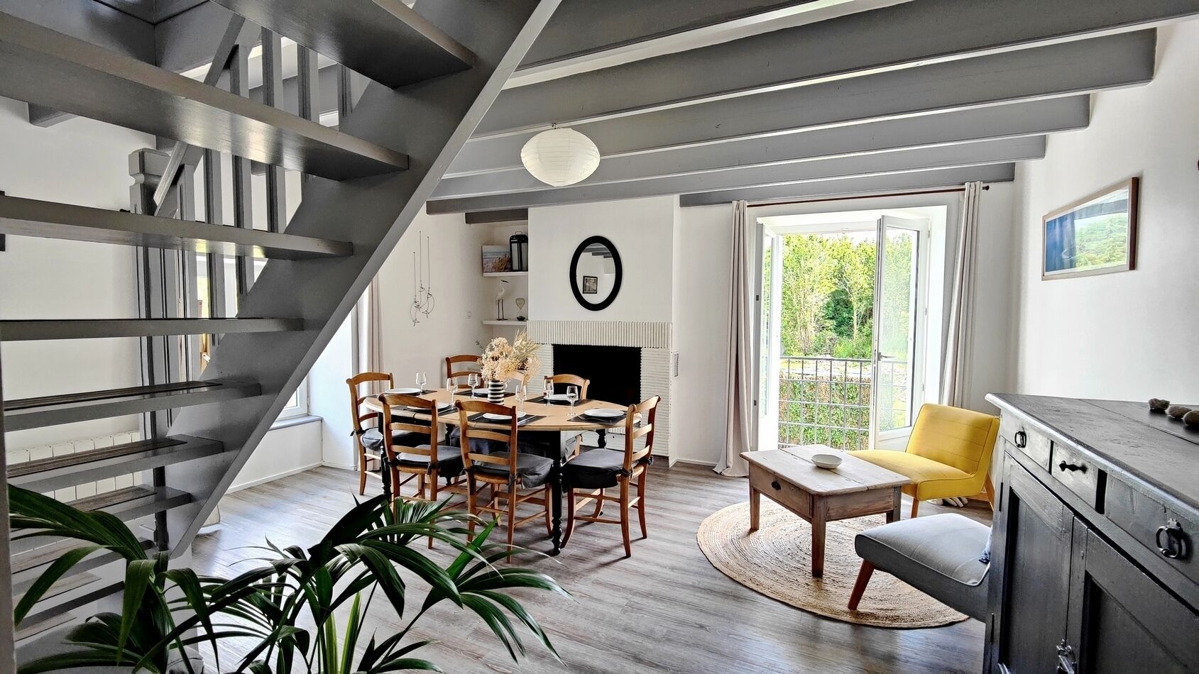 A modern interior with a staircase, dining area, and a view through a large window.