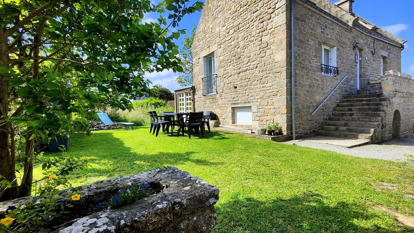A stone building with a grassy yard, outdoor seating, and a staircase leading to the entrance.