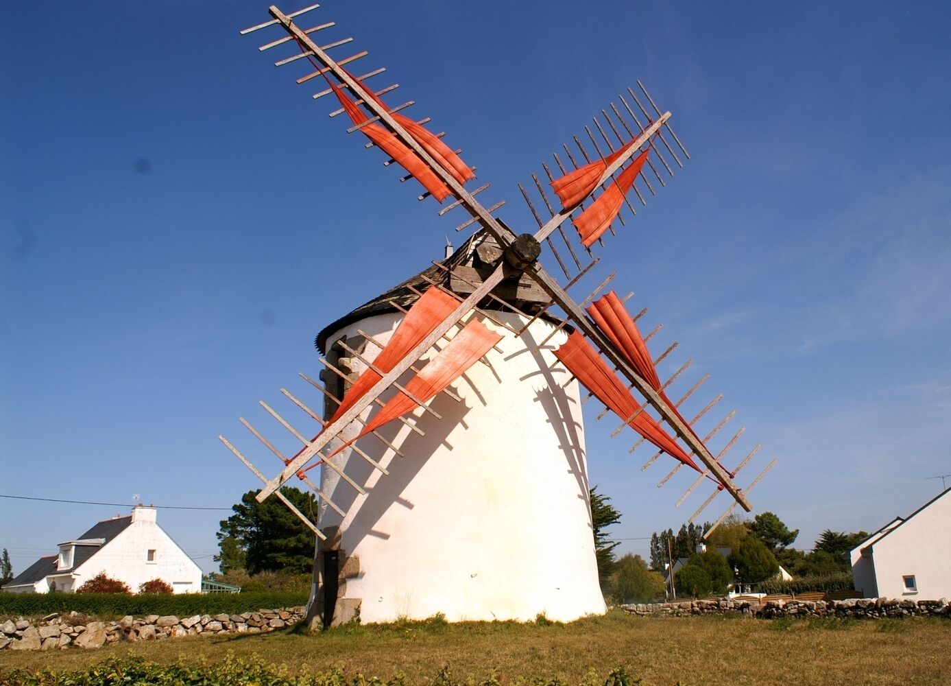 A windmill with wooden sails, a white body, and a stone base.
