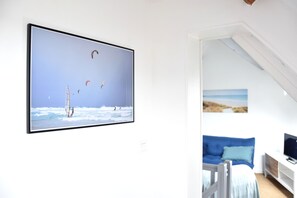 A room with a large TV mounted on the wall displaying a beach scene with windsurfing. - Renovated old barn in Erdeven (sleeps 6–8) 500 m from the beaches, with a garden (Erdeven)