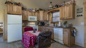 A compact kitchen with wooden cabinets, a microwave, a refrigerator, and a dining area with a table covered in a red tablecloth. - Tree House Suite at the Calhoun House Inn & Suites (Bryson City)