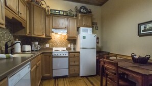 A compact kitchen with wooden cabinets, a stove, a microwave, and a refrigerator. - Toy Box Suite at the Calhoun House Inn & Suites (Bryson City)