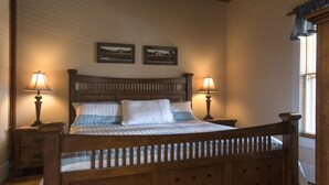 A wooden bed with a headboard, two bedside lamps, and two framed pictures on the wall. - Toy Box Suite at the Calhoun House Inn & Suites (Bryson City)