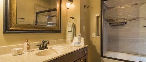 A bathroom with a large mirror, two sinks, a shower, and a towel rack.