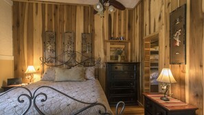 Une chambre avec un mur lambrissé en bois, un lit avec un cadre en métal, une commode et une table de chevet avec une lampe.