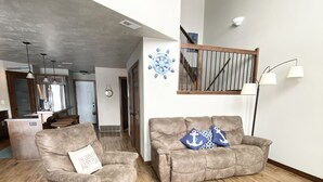 A spacious living room with a wooden floor, two sofas, a coffee table, and a staircase leading to an upper level.