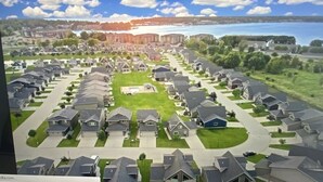 A residential area with houses arranged in rows, a central green space, and a body of water in the background.