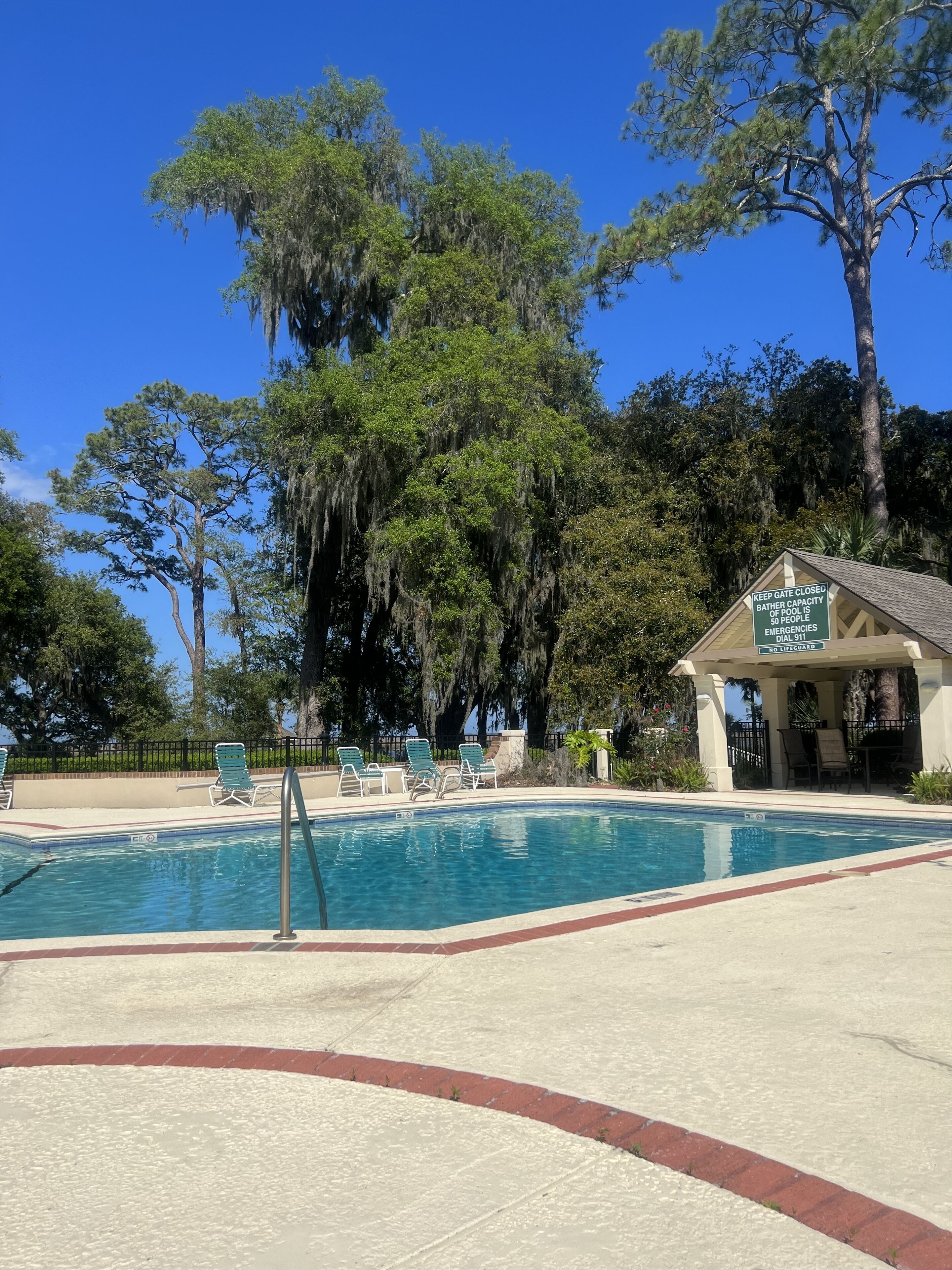 A swimming pool with lounge chairs, a lifeguard station, and trees in the background.
