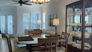 A dining area with a round table, chairs, a chandelier, a ceiling fan, and a glass display cabinet with china. - Private and quiet condo on North end of SSI. 30 day minimum. 
 (St. Simons Island)