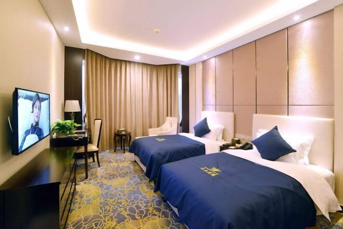 A hotel room with two beds, a TV, a desk, and a chair.
