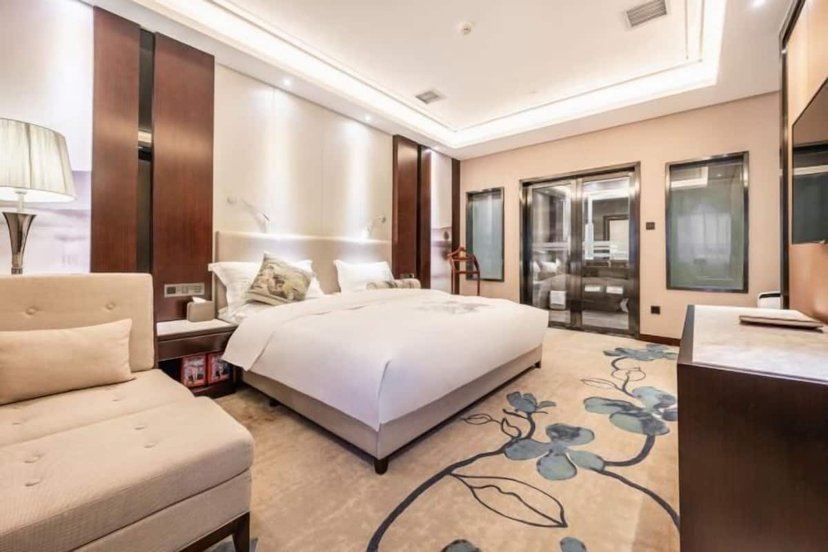 A modern hotel room with a large bed, a sofa, a desk, and a bathroom with a glass door.