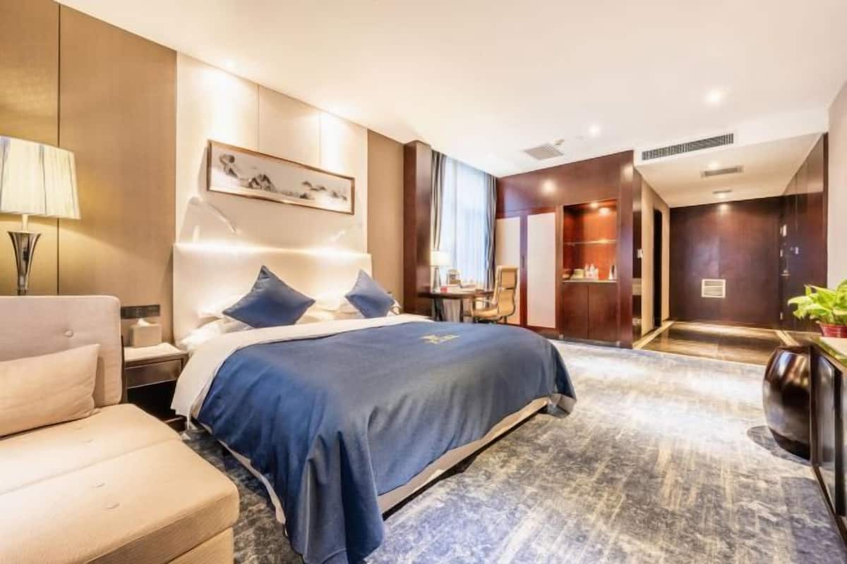 A modern hotel room with a large bed, a bedside table, a desk, and a chair.