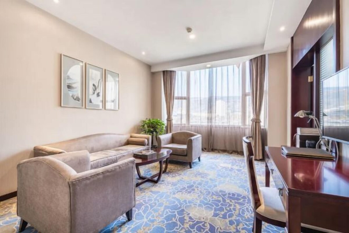 A hotel room with a sofa, armchairs, a dining table, and a TV.