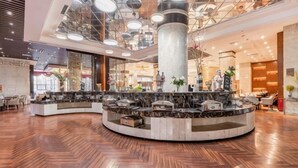 Un vestíbulo de hotel con una recepción central, un techo alto con iluminación circular y un piso de madera.