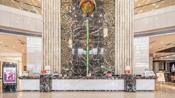 A hotel reception area with a marble reception desk, a large decorative wall, and a high ceiling.