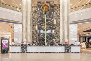 A hotel reception area with a marble reception desk, a large decorative wall, and a high ceiling.