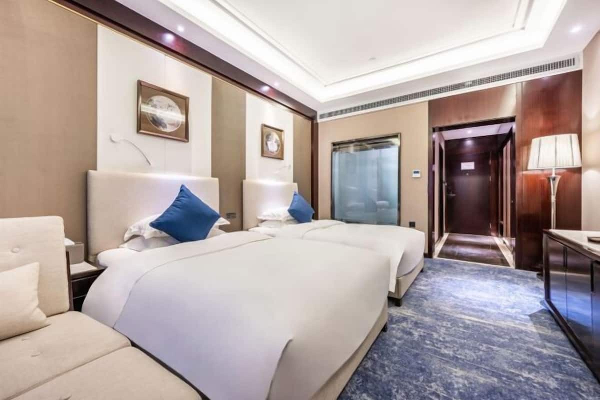 A hotel room with two beds, a sofa, a desk, and a bathroom door.