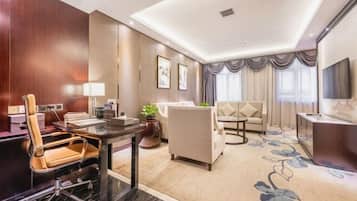 A hotel room with a dining area, a sofa, a TV, and a large window with curtains.