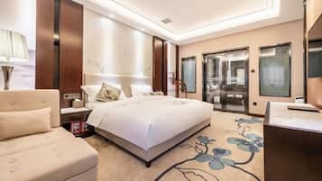 A modern hotel room with a large bed, a sofa, a desk, and a bathroom with glass doors.