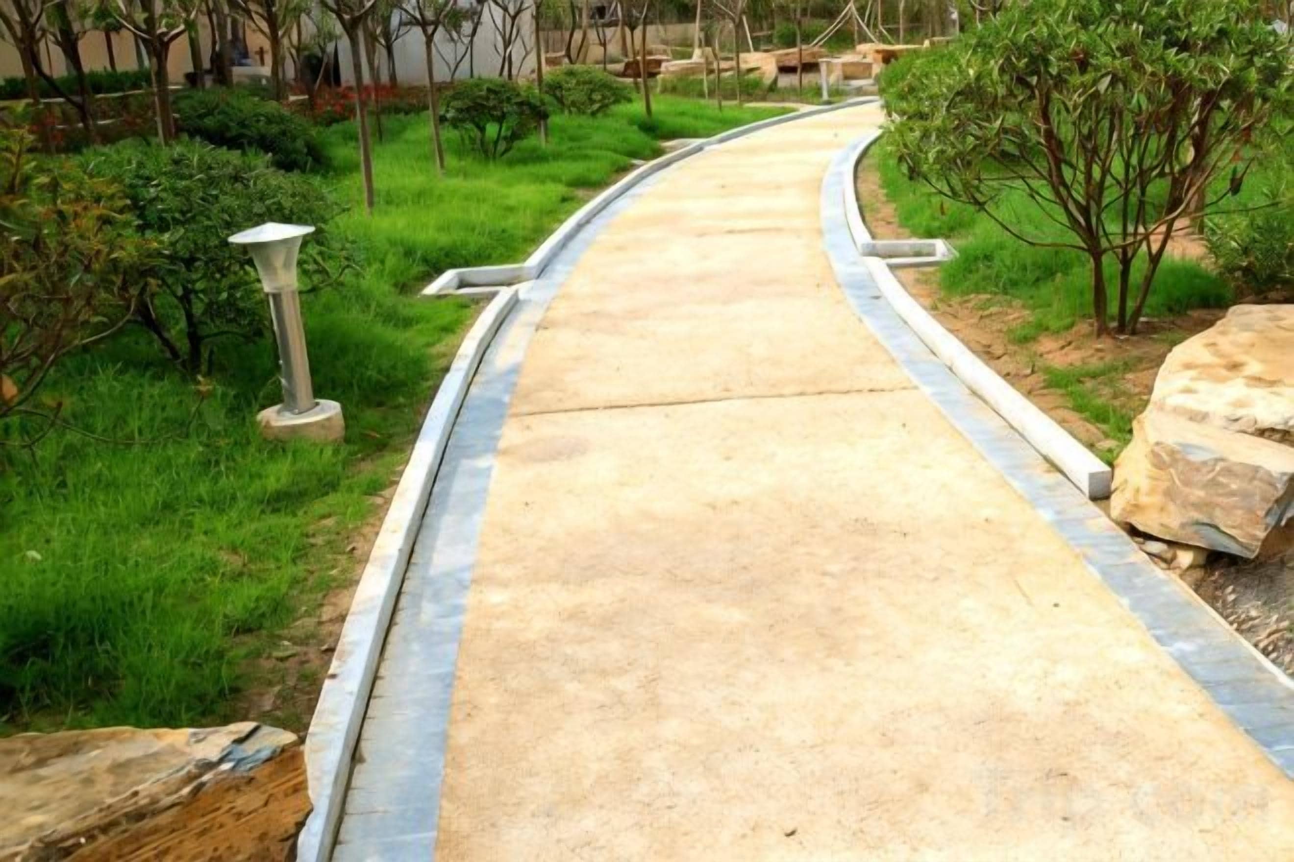 A curved concrete pathway bordered by grass and small trees, leading to a building entrance.