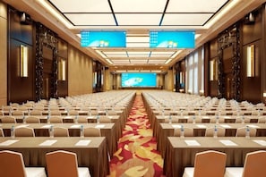 A conference room with rows of tables and chairs, a carpeted floor, and a large screen at the front.