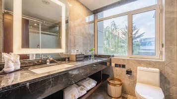 A modern bathroom with a large mirror, two sinks, a toilet, and a window providing a view of the outdoors.