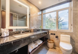 A modern bathroom with a large mirror, two sinks, a toilet, and a window providing a view of the outdoors.