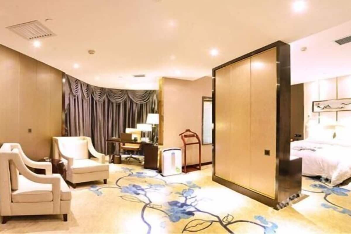 A hotel room with a bed, two armchairs, a desk with a lamp, a wardrobe, and a carpet with a floral pattern.