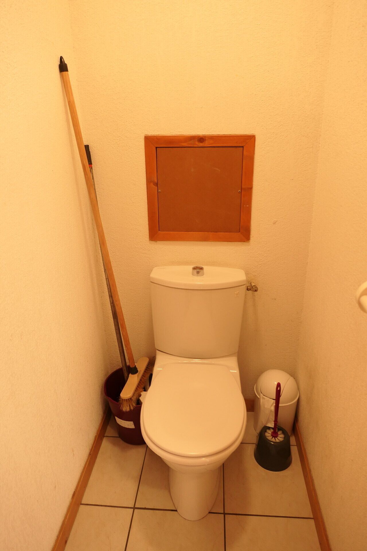Ein kleines Badezimmer mit Toilette, einem Holzbürste, einem Kehrblech und einem Pömpel.