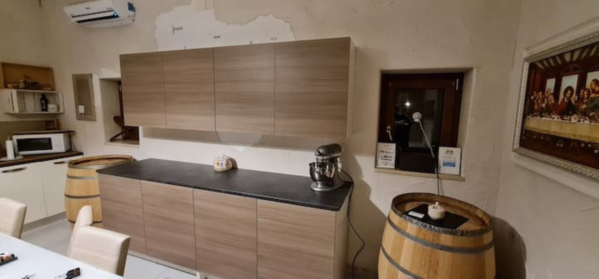 Une cuisine avec des meubles de rangement en bois, un plan de travail noir, un four à micro-ondes et un tonneau en bois.