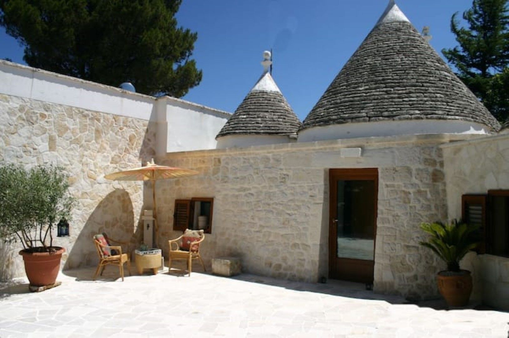 A stone building with a tiled roof, a door, and a small patio area with a chair and a table.