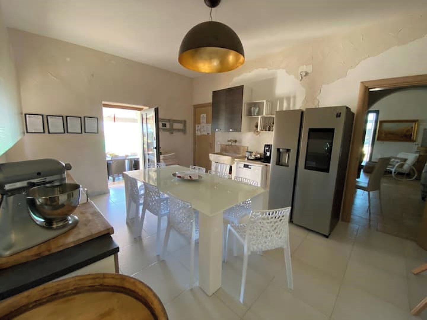 A modern kitchen with a central island, white chairs, a large refrigerator, and a hanging light fixture.