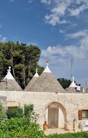 A stone building with a central arched doorway, surrounded by greenery and a clear sky.