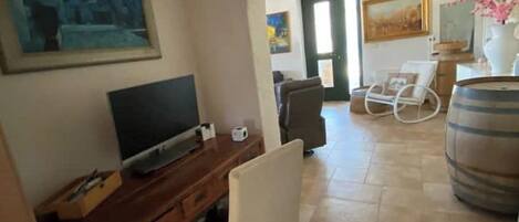 Un salon avec un téléviseur, un bureau et une chaise. Une porte donne accès à une autre pièce.