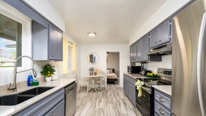 A compact kitchen with grey cabinets, stainless steel appliances, and a small dining area with a table and chairs. - Old Town 4BR Gem | Pool, Firepit, WiFi, & Games! (Scottsdale)