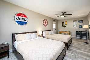 A hotel room with two beds, a ceiling fan, and various wall decorations including a Jeep logo and a Texaco logo.