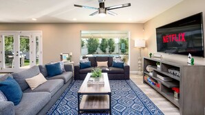 A modern living room with a grey sofa, a coffee table, and a TV displaying 'NETFLIX'. - Old Town 4BR Gem | Pool, Firepit, WiFi, & Games! (Scottsdale)