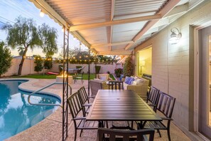 An outdoor patio with a pool, a covered seating area, and a fire pit.