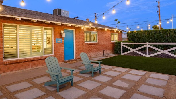 Uma casa de tijolos com porta azul, duas cadeiras Adirondack e luzes de Natal.