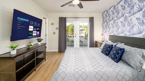 Quarto com cama, TV fixada na parede, ventilador de teto e vista para o exterior através de uma porta de vidro.